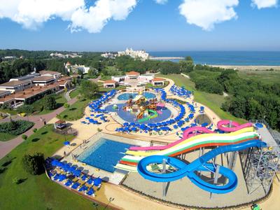 Vodní park s několika bazény, tobogány a lehátky vedle hotelu a pláže.