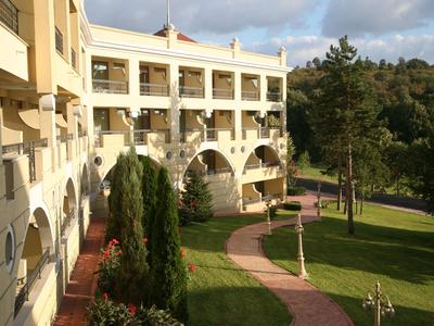 Hotelová budova s balkonem a dlážděnou cestou přes zelenou zahradu za slunečného dne