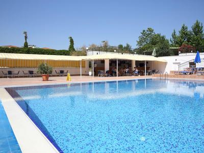 Groot buitenzwembad met zitgedeelte en parasols voor een wit gebouw onder een blauwe lucht.