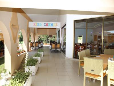 Licht hotelgang met tafels, stoelen en een kleurrijke kinderspeelhoek.