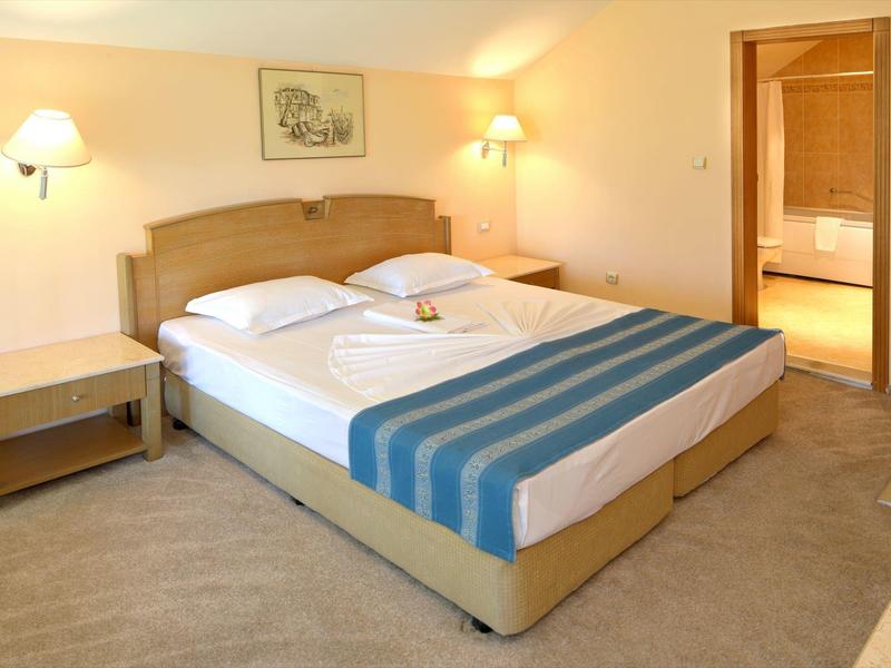 Lichte hotelkamer met tweepersoonsbed, nachtkastjes en uitzicht op een badkamer.