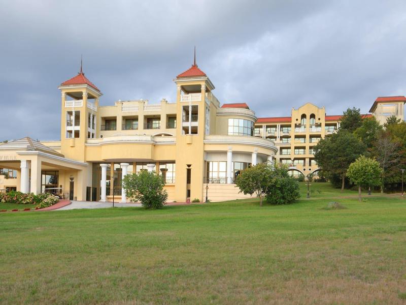 Groot hotelgebouw met gele gevel onder bewolkte lucht en groot groen gazon op de voorgrond