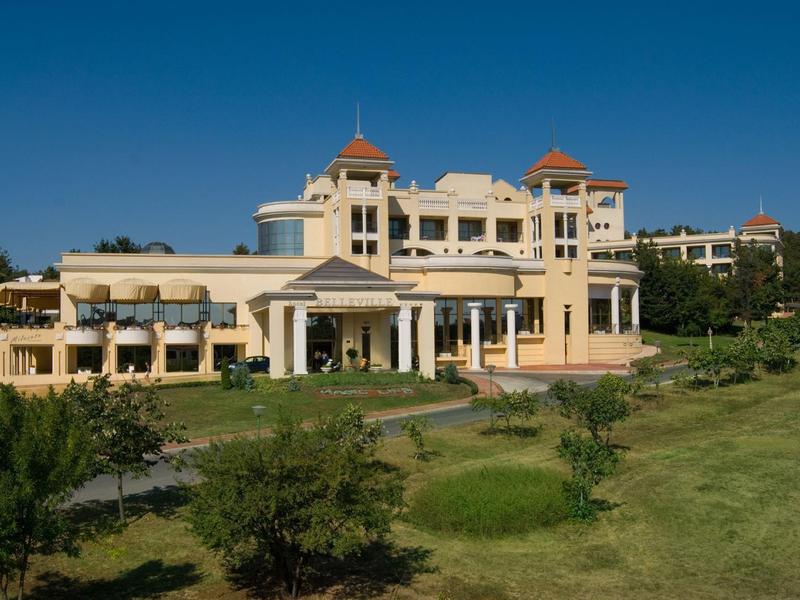 Groot elegant hotelgebouw onder een heldere blauwe lucht met verzorgde tuin