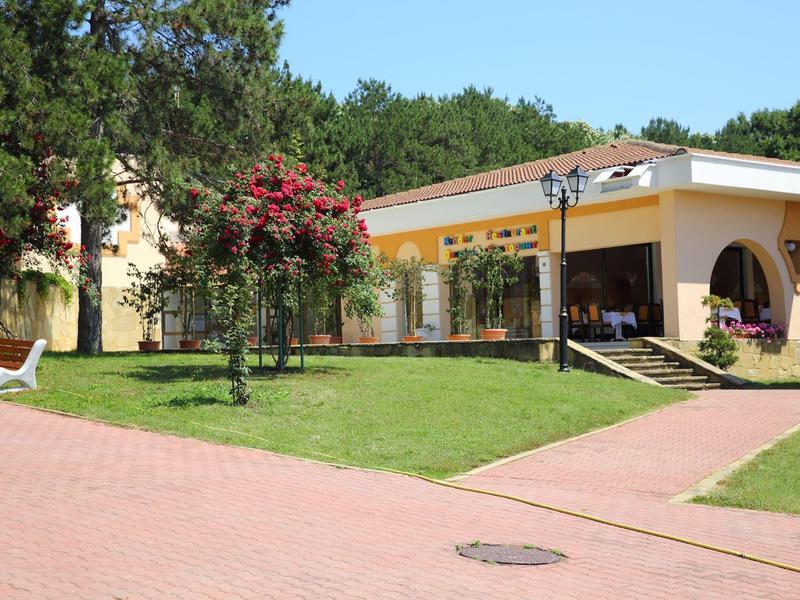 Hotelgebouw met tuin, rode bloemenstruik en parasol bij zonnig weer