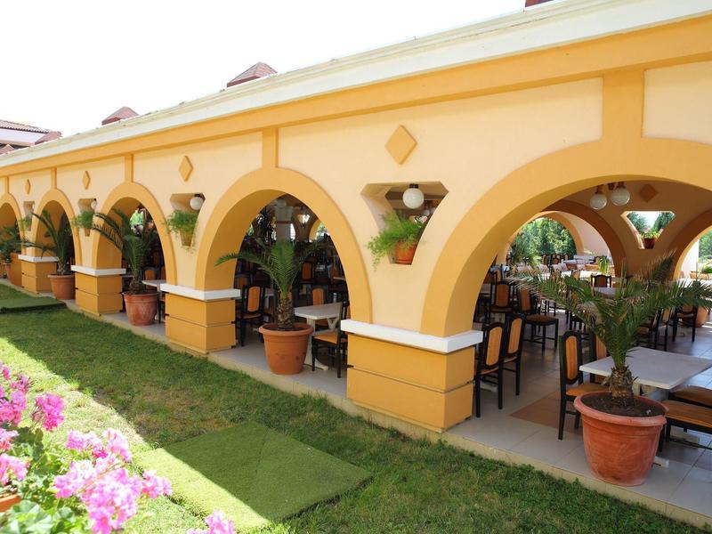 Geel gebouw met bogen en terras omringd door bloemen en gras