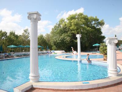 Ein Pool mit weißen Säulen, umgeben von Bäumen und Sonnenschirmen bei klarem Himmel.