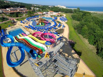Wasserpark mit Rutschen, Pools und Liegestühlen nahe einem Hotel und einem Waldgebiet am Meer.
