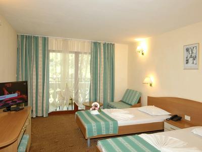 Camera d'albergo luminosa con due letti singoli, TV, scrivania e balcone con vista sugli alberi.