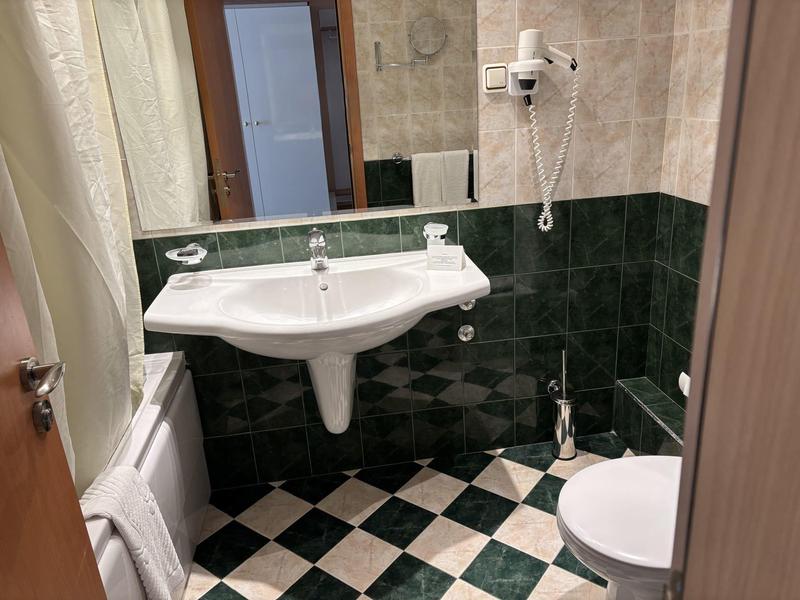 Piccolo bagno con lavabo bianco, WC, asciugacapelli e pavimento a scacchiera bianco e nero.