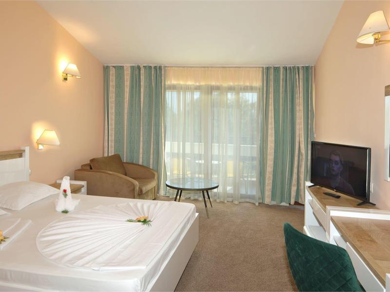 Camera d'hotel luminosa con letto grande, poltrone, TV e balcone con tende.