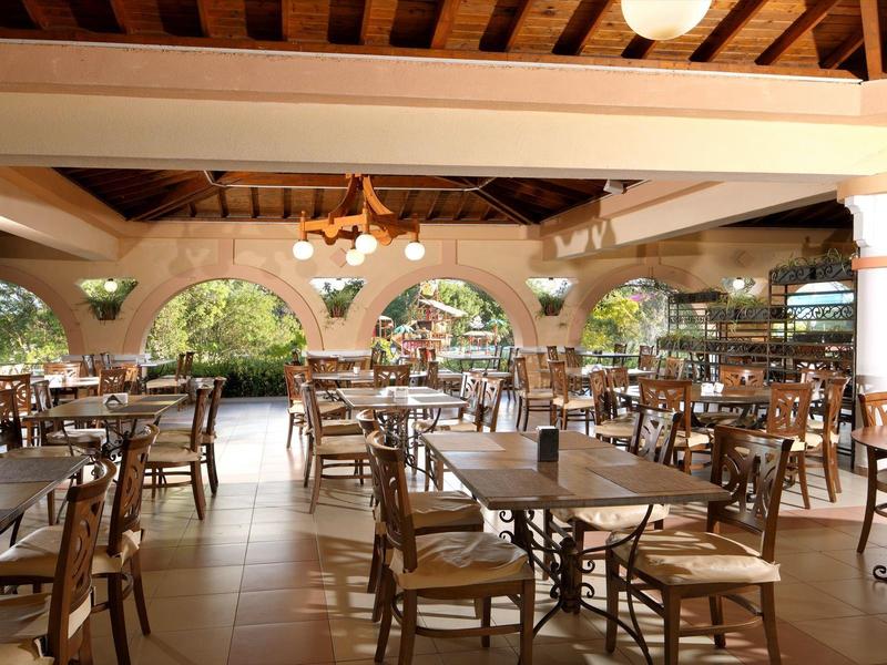 Area pranzo aperta con tavoli e sedie in legno sotto un soffitto con travi in legno