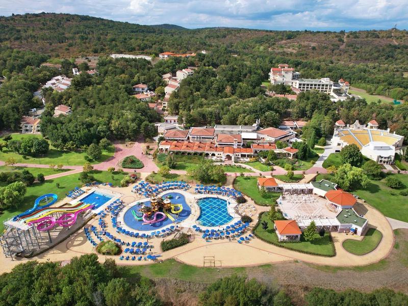 Vista di un resort con più piscine circondato da paesaggio verde e colline.