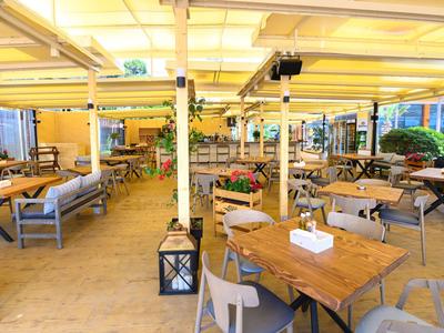 Krytá venkovní terasa s dřevěnými stoly a židlemi v restauraci nebo kavárně.