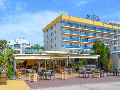 Velká hotelová budova s jasnou fasádou a otevřenou venkovní restaurací za slunečného počasí.