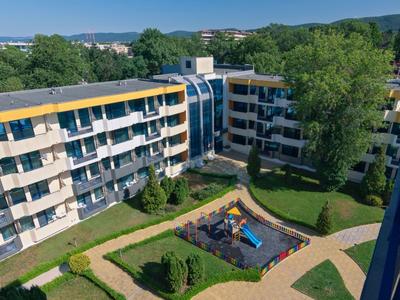 Vícepodlažní hotelová budova s hřištěm a zelenými plochami za slunečného počasí