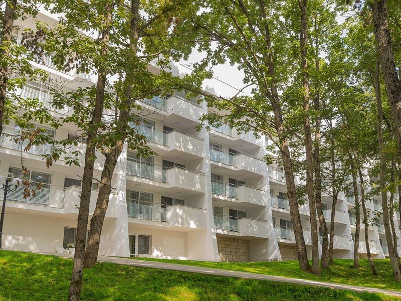 Modern apartment building with balconies surrounded by green trees and grass.
