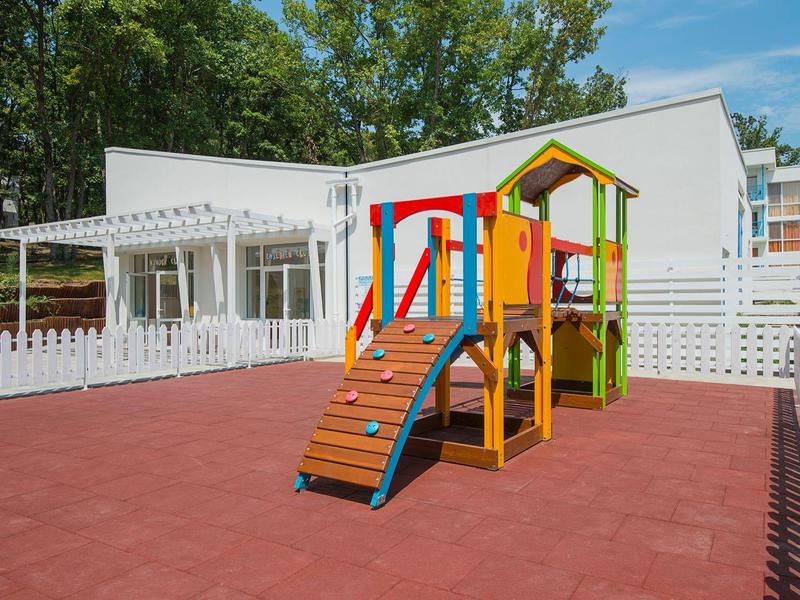 Colorful children's playground with slide next to modern building and fence.