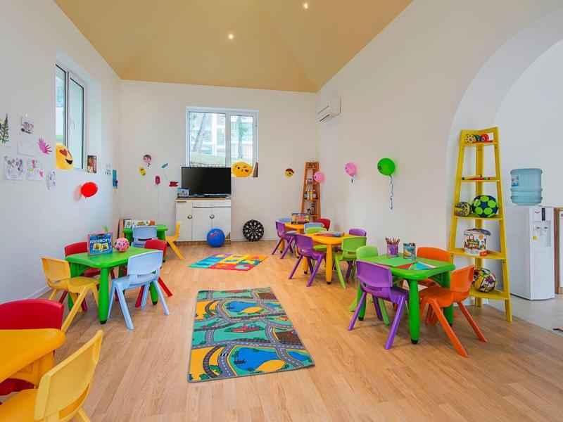 Colorful playroom with small tables, chairs, and wall decorations in a bright space.
