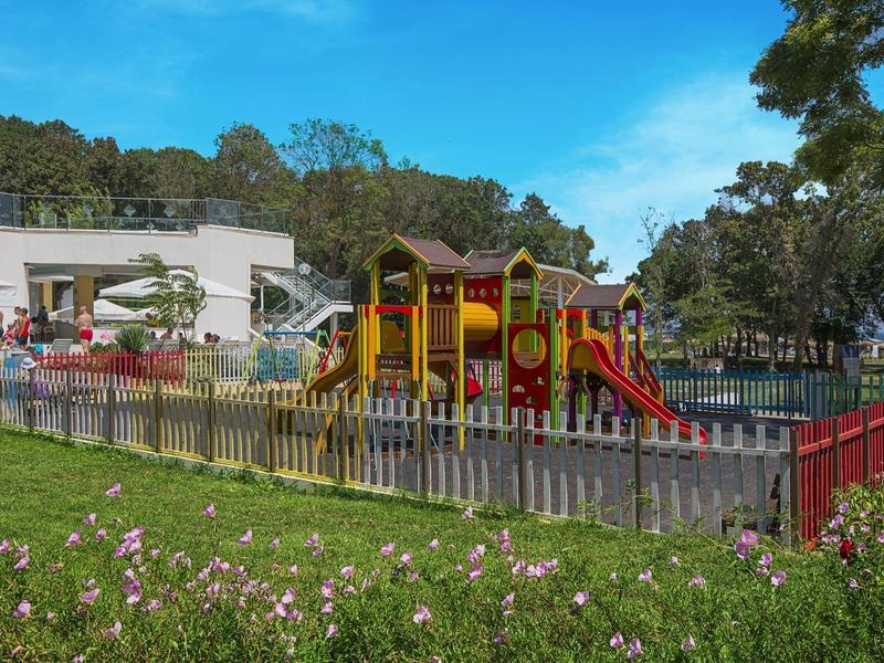 Colorful playground with slide and climbing frame in front of a hotel building under blue sky.
