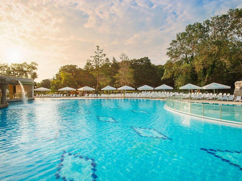 Large hotel pool with sun umbrellas and loungers at sunset