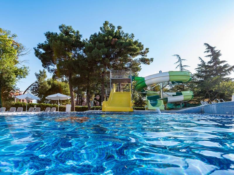 Water park with colorful water slides and a blue swimming pool, surrounded by trees and umbrellas.