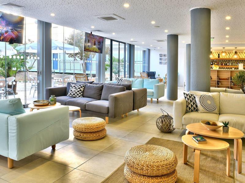 Bright hotel lounge with large window, cozy sofas, and round poufs.