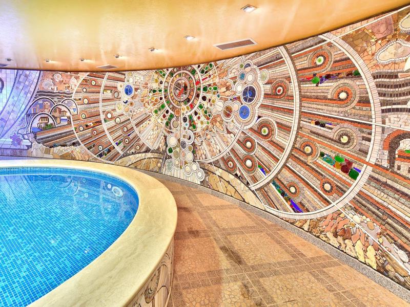 Indoor pool with colorful, artistic wall mosaic and rounded pool edge.