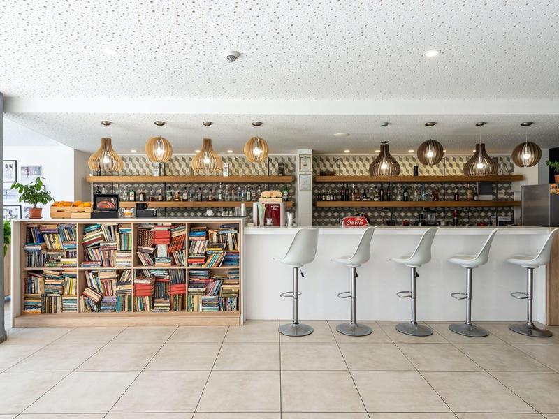 Modern hotel bar area with white bar stools and bookshelves in the background.