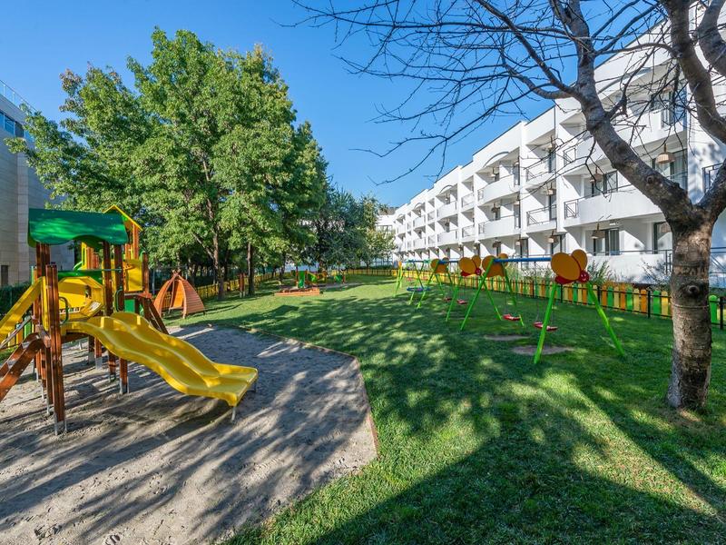 Playground with slide and swings next to a hotel building in greenery