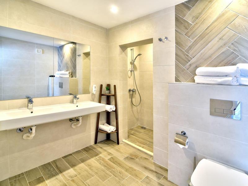 Modern hotel bathroom with double sinks, rain shower, and white towels.