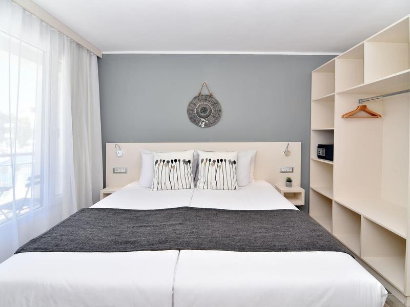 Bright hotel room with double bed, large windows, and open wardrobe.