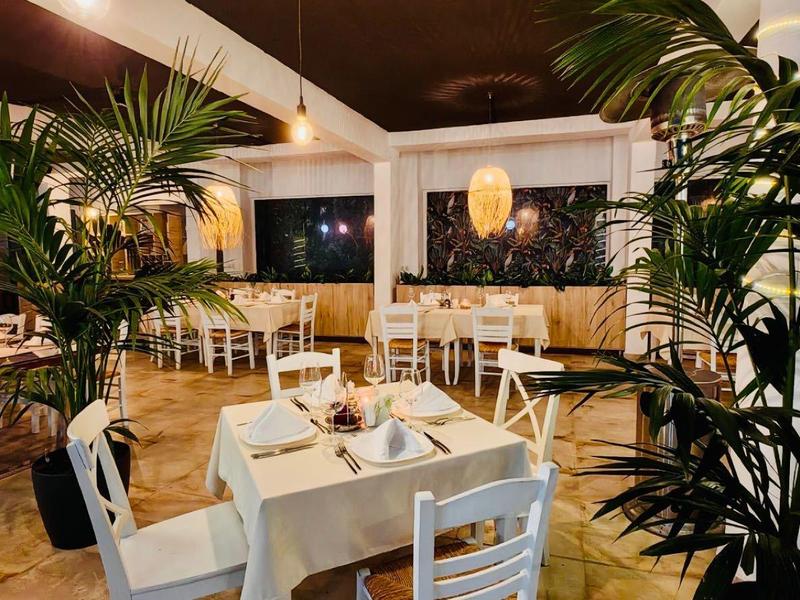 Elegant restaurant with white tables, plants, and ambient lighting.