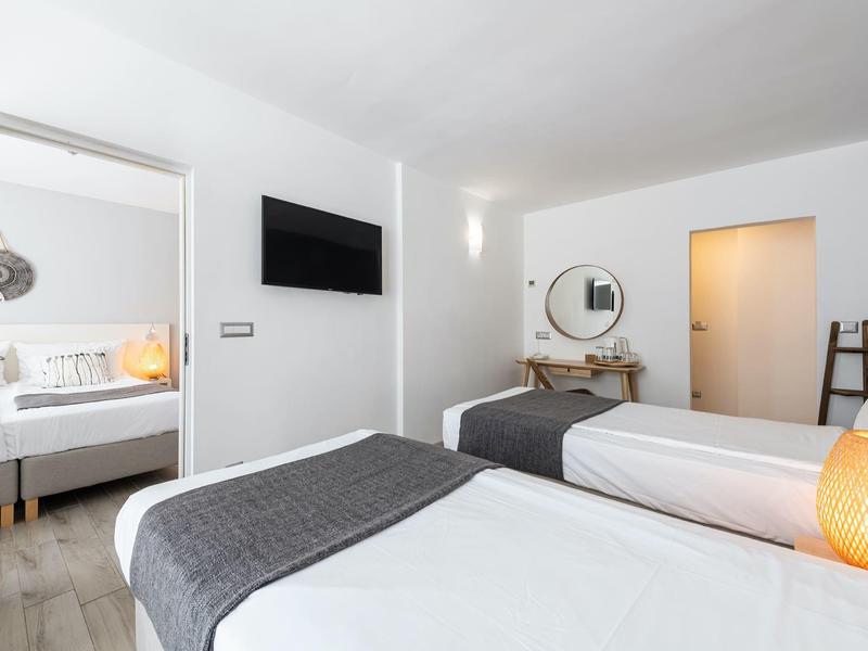 Modern hotel room with two single beds, TV, and dresser with round mirror.