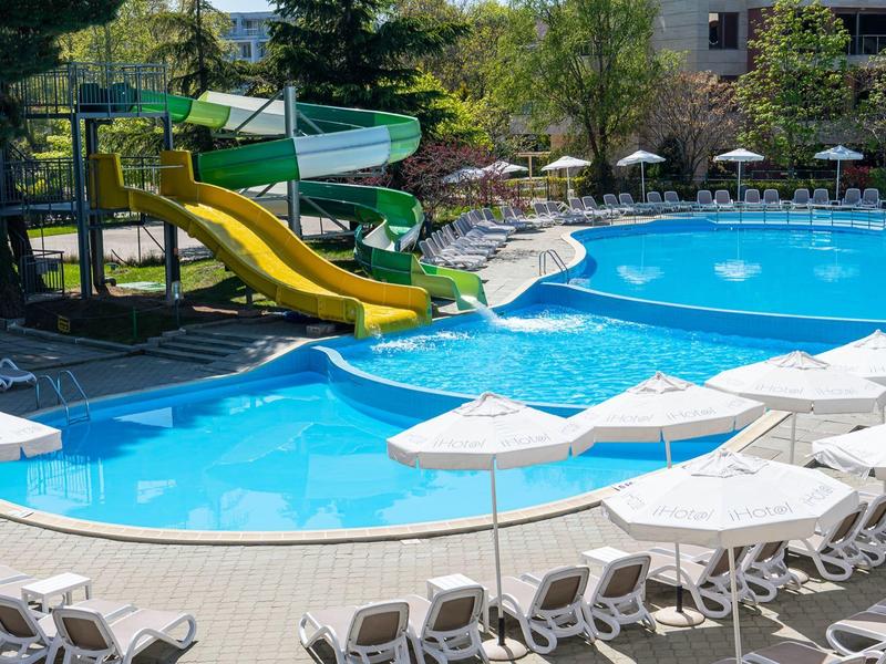 Hotel pool with water slides, umbrellas, and sun loungers outdoors.