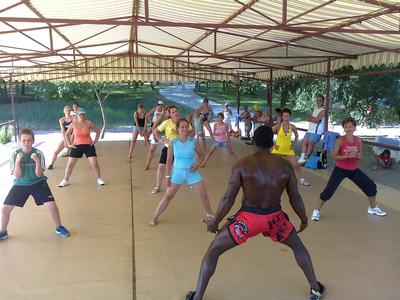 Gruppen-Fitnesskurs im Freien unter einem Dach mit Teilnehmern in sportlicher Kleidung.