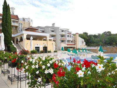 Hotel mit Außenpool, umgeben von bunten Blumen und mehreren Sonnenschirmen.
