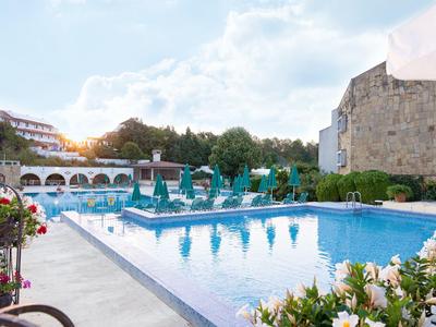 Hotelpool mit Liegestühlen und Sonnenschirmen, umgeben von Blumen und Gebäuden bei Sonnenuntergang.