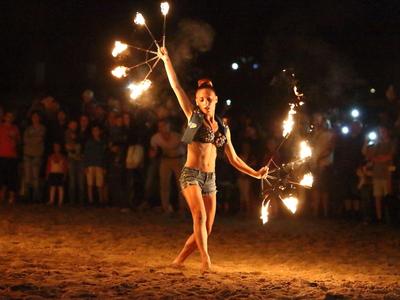 Frau führt Feuershow am Strand vor Publikum in der Nacht auf.