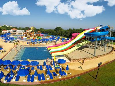 Piscina colorata con scivoli e lettini blu in un parco acquatico sotto il sole.
