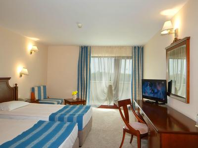 Camera d'hotel con due letti singoli, coperte blu e bianche, scrivania e balcone con tende.