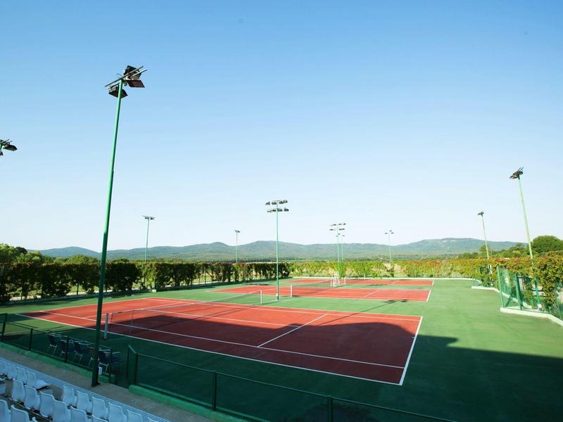 Campi da tennis all'aperto con superficie rossa sotto un cielo sereno e ambiente verde.