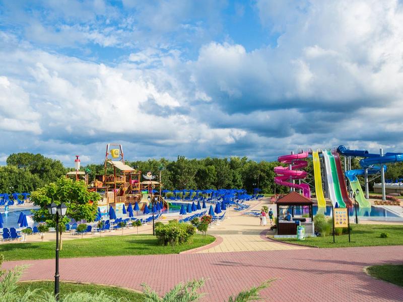 Parco acquatico con scivoli colorati e sedie a sdraio blu sotto un cielo nuvoloso.