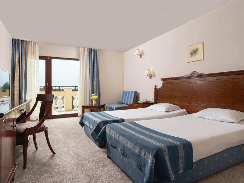 Camera d'hotel con due letti singoli, mobili in legno e balcone con vista esterna