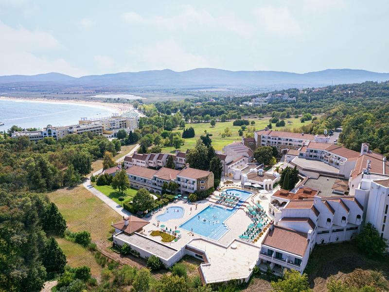 Complesso alberghiero con piscina vicino a una spiaggia e colline boschive sullo sfondo