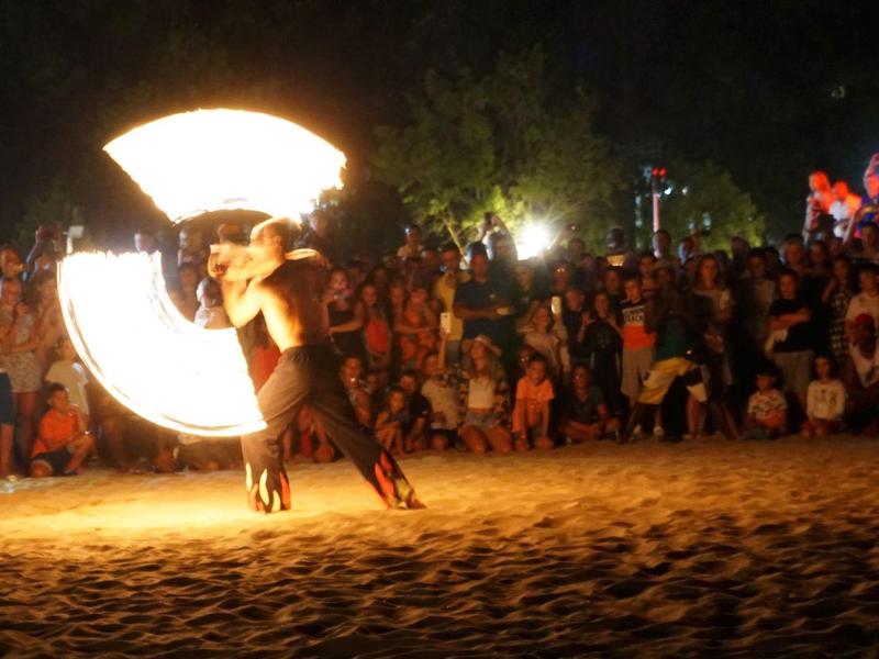 Spettacolo di fuoco sulla spiaggia di notte con molti spettatori sullo sfondo.