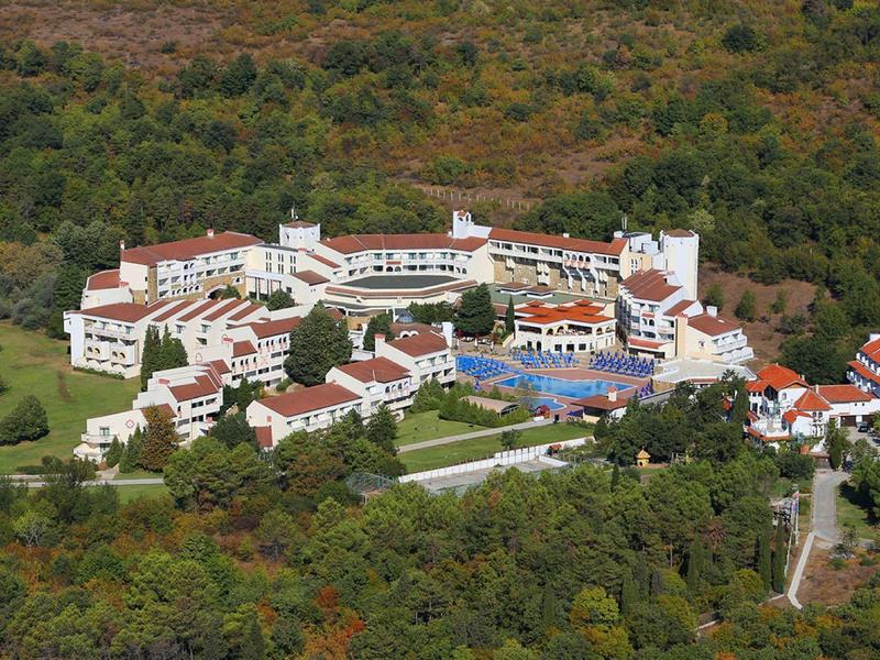 Grande complesso alberghiero con più edifici e piscine, circondato da una fitta foresta.
