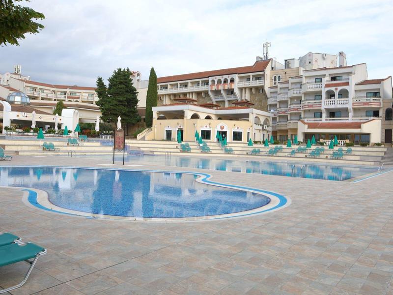 Grande piscina dell'hotel con sedie a sdraio e edifici su più piani sullo sfondo.
