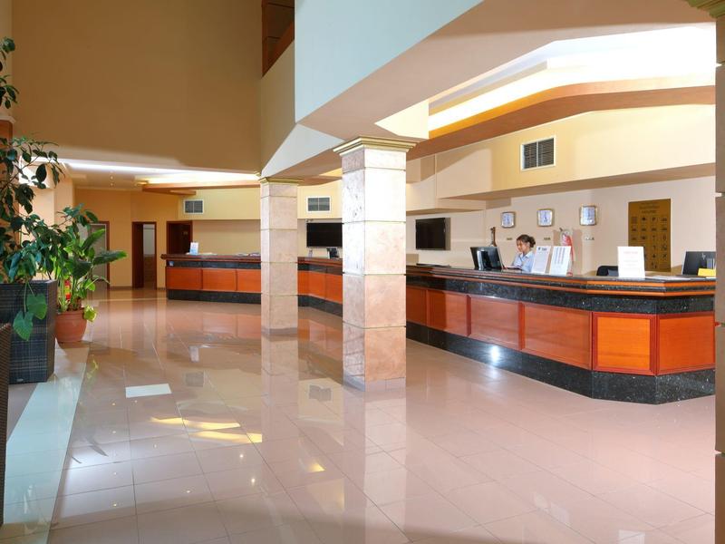 Moderna hall dell'hotel con reception, pavimento lucido e alcune piante.