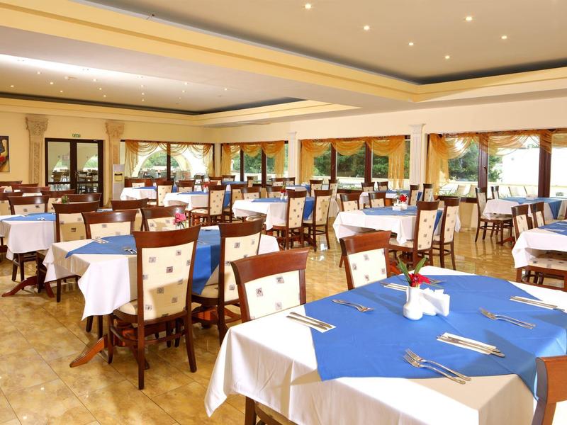 Ampia e luminosa sala da pranzo con molti tavoli e sedie, apparecchiata con tovaglie blu e bianche.