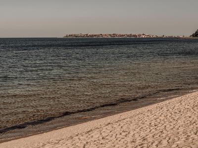 Klarig zandstrand met rustige zee en een verre landtong aan de horizon.